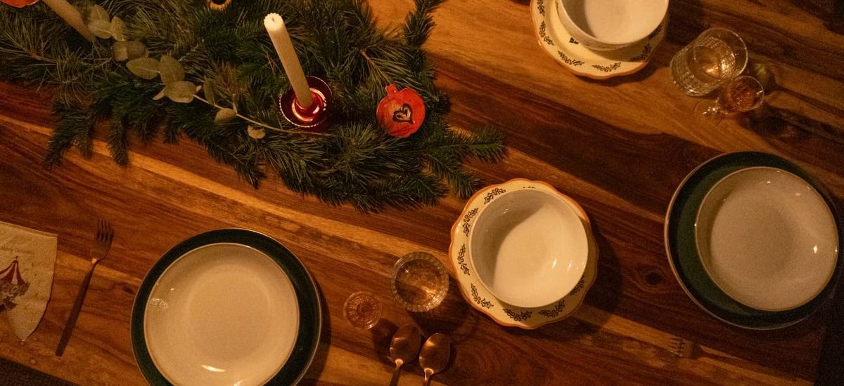 Warm and inviting Christmas table setup with candles and pine decor on wooden surface.
