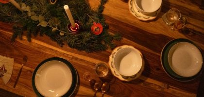 Warm and inviting Christmas table setup with candles and pine decor on wooden surface.