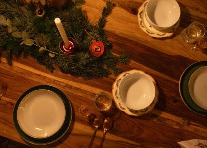 Warm and inviting Christmas table setup with candles and pine decor on wooden surface.