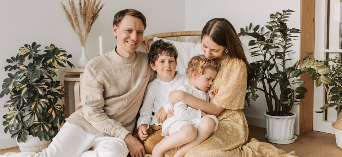 Happy family of four enjoying quality time together in a cozy, plant-filled room.