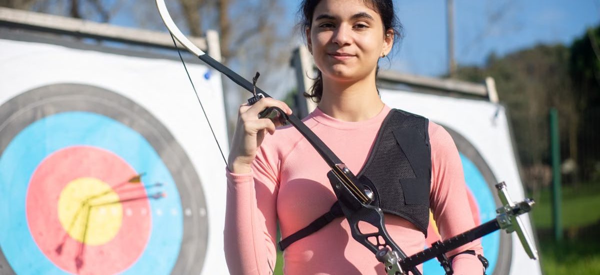 Confident young woman practicing archery in Portugal, showcasing skill and focus in outdoor setting.