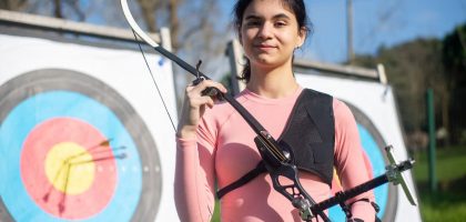 Confident young woman practicing archery in Portugal, showcasing skill and focus in outdoor setting.