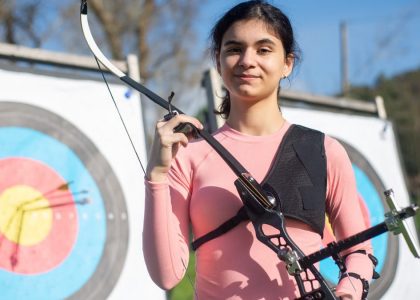 Confident young woman practicing archery in Portugal, showcasing skill and focus in outdoor setting.